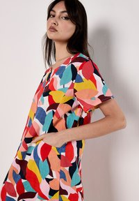 Buntes kurzärmeliges Kleid mit einem Blättermuster in Rot, Orange, Pink, Türkis und Marineblau auf weißem Hintergrund; enthält seitliche Taschen.