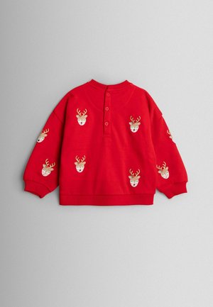 Červená mikina s výšivkou hlav jelenů s parohy. Kolačičkový výstřih, dlouhé rukávy s elastickými manžetami, volný střih. Knoflíková úprava na krku.