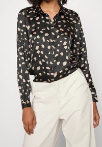 Blusa nera in satin con motivo a macchie beige e marrone chiaro, maniche lunghe, design con colletto e chiusura con bottoni.