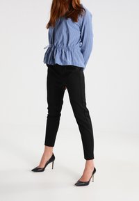 Blusa a righe blu e bianche con vita cin cin, abbinata a pantaloni neri aderenti e scarpe nere con tacco alto.