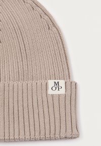 Knit beanie in light beige with a ribbed texture. Features a small label with "M O' P" on the cuff. Soft material. Classic design.