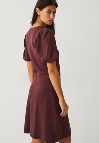 Bordeauxfarbenes Kleid mit Puffärmeln, tailliertem Bund und ausgestellt Rock. Weiche Textur, knielang, minimale Nähte und runder Ausschnitt.