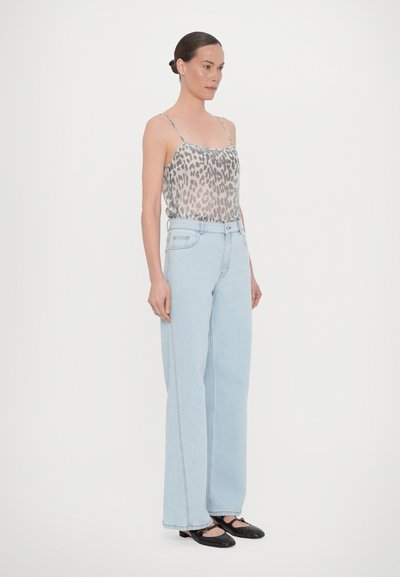 Top mit Leopardenmuster und Spaghettiträgern, hochgeschnittene hellblaue weit geschnittene Jeans und schwarze Schuhe mit strukturiertem Akzent, getragen von einem Model.