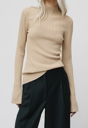 Beżowy prążkowany top z długim rękawem i wysokim dekoltem oraz wydłużonymi rękawami, połączony z ciemnozielonymi szerokimi spodniami.