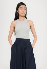 Graues geripptes Tanktop mit hohem Kragen, kombiniert mit einem marineblauen gefältelten Rock mit Streifen und seitlichen Taschen.