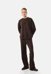 Bruine oversized sweatshirt met een ronde halslijn en subtiele graphic, gecombineerd met bijpassende wijdvallende broek en gezellige slippers.