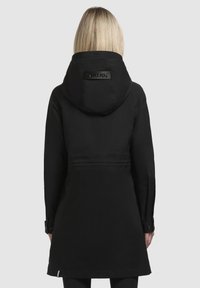 Black waterproof parka featuring a hood, cinched waist, buttoned cuffs, and textured fabric. Branding visible on the back yoke.
