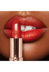Red lipstick in a gold tube applied to full, glossy lips. The lipstick has a kiss print on its side and a smooth texture.