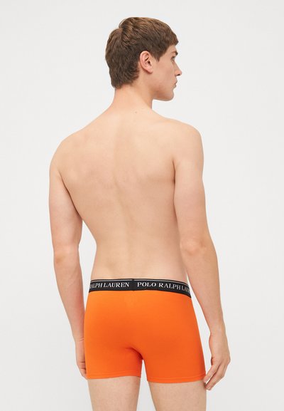 Oranžne bokserice z črnim elastičnim pasom, na katerem je napis "POLO RALPH LAUREN", izdelane iz gladkega materiala, prilegajoče zasnove. Zadnji pogled.