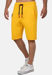 Gele sportshorts gemaakt van zachte stof, met een elastische tailleband met zwarte trekkoorden en zijzakken.