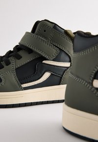 Baskets montantes en cuir noir et vert olive, dotées d'une bride à scratch, de coutures contrastantes et d'une semelle en caoutchouc de couleur crème.