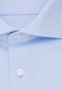 Lichtblauwe kraag met knoopsluiting. Heeft een gestructureerde stof en een gladde afwerking, wat de scherpe lijnen en gestructureerd ontwerp benadrukt.