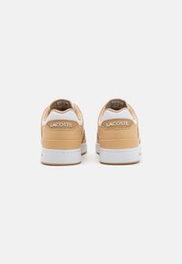 Lacoste-sneakers med en beige ovandel, vita detaljer, slätt läder, texturerad baksida och en gummisula. Logotyp präglad på hälen.