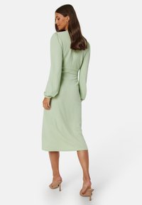 Abito midi verde menta con texture, maniche lunghe a sbuffo, vita aderente e gonna svasata, abbinato a sandali con tacco nude.
