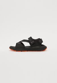 Schwarze Sandalen mit orangefarbenen Außensohlen, ausgestattet mit verstellbaren Riemen, einem eleganten Design und einem strukturierten Obermaterial für besseren Halt.