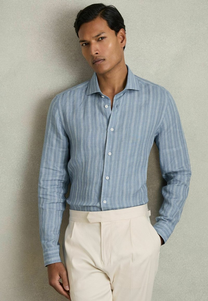 Blauw gestreepte blouse met lange mouwen van lichte stof, met een button-down kraag, gecombineerd met crèmekleurige plooibroek.