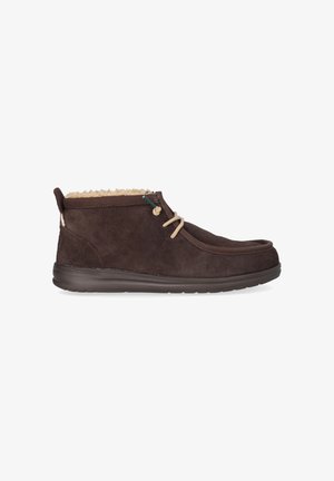 Bottine en daim marron avec une doublure douce couleur tan, bout arrondi, design à lacets et semelle en caoutchouc texturée basse. Dotée d'une languette à l'arrière.