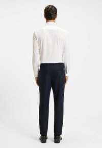 White long-sleeve shirt with button cuffs and dark navy trousers. Smooth fabric with a tailored fit. Black dress shoes completing the outfit.