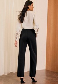 Crème blouse met kanten manchetten, gecombineerd met hoge zwarte broeken en zwarte hakken. Soepele texturen, elegante uitstraling en op maat gemaakte pasvorm.