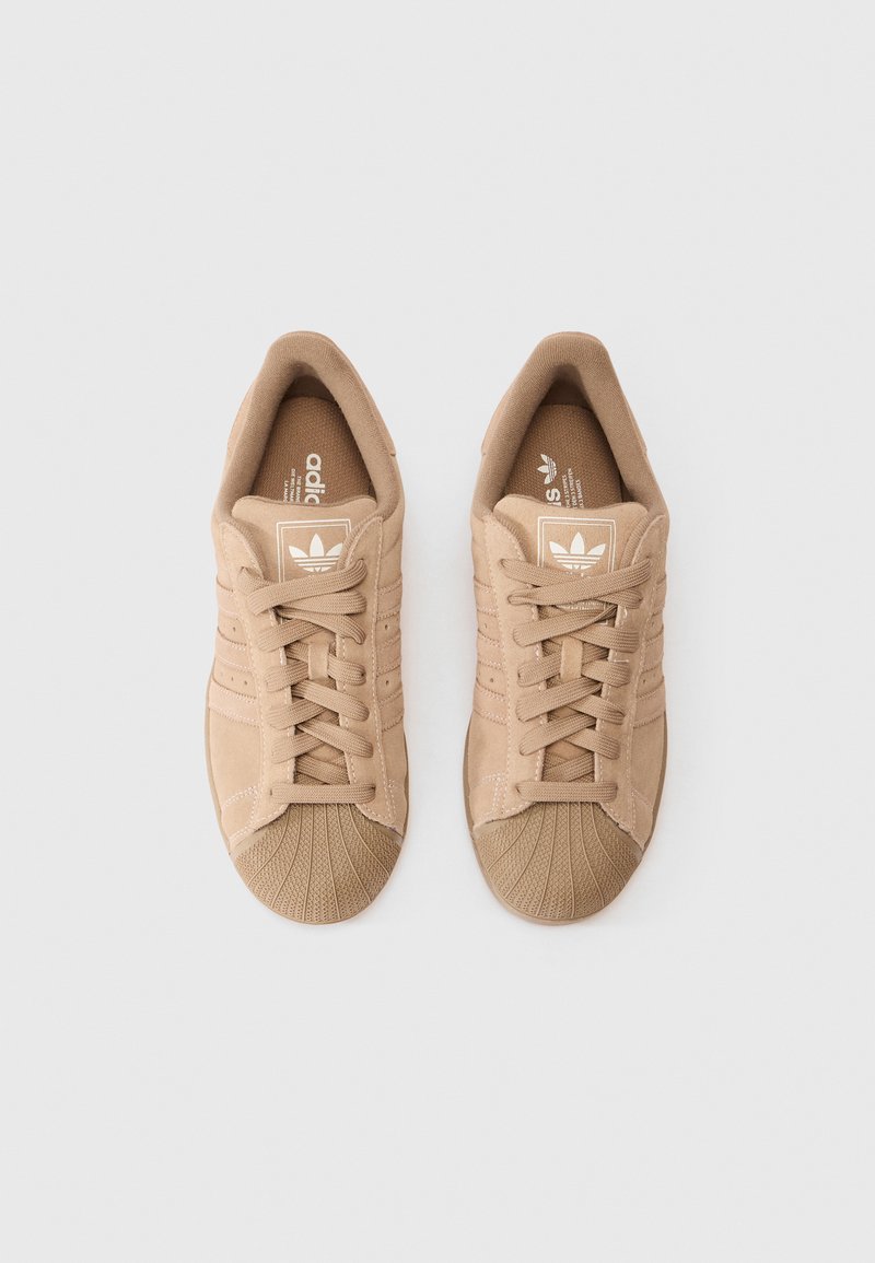 Baskets en suede beige avec un embout en caoutchouc texturé, dotées de lacets plats, d'un intérieur doux et du logo Adidas sur la languette.