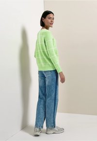 Pull en maille vert avec des rayures blanches, col rond, coupe oversize, associé à un jean en denim bleu clair et des baskets argentées.