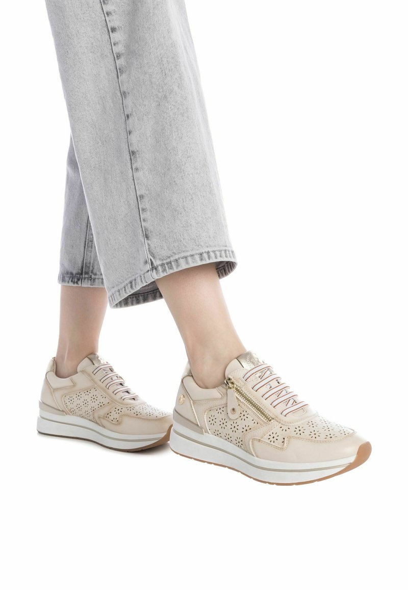 Zapatillas de cuero beige con diseño perforado, detalles en dorado y suela blanca gruesa. Cordones en varios colores y cremallera lateral funcional.