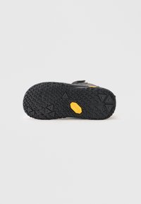 Suola di scarpa nera da esterno con un motivo testurizzato per la presa; presenta un logo giallo e una costruzione in gomma per la durabilità.