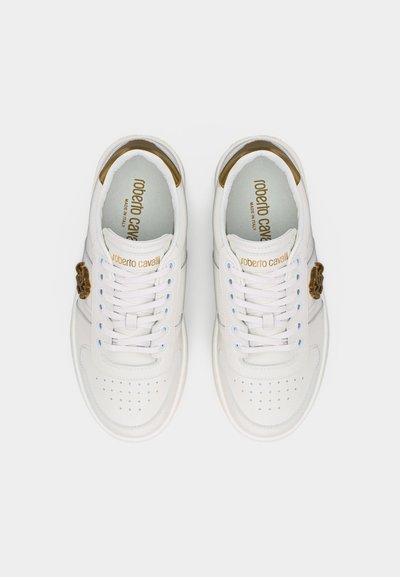 Ζευγάρι λευκών αθλητικών παπουτσιών Roberto Cavalli με χρυσό λογότυπο στη γλώσσα και χρυσό διακοσμητικό έμβλημα στις εξωτερικές πλευρές, δεμένα και ορατά από πάνω.