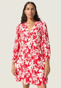 Vestido rojo con flores que presenta un escote en V, mangas largas abullonadas y un corte holgado. La tela tiene una apariencia suave y texturizada con patrones florales blancos.
