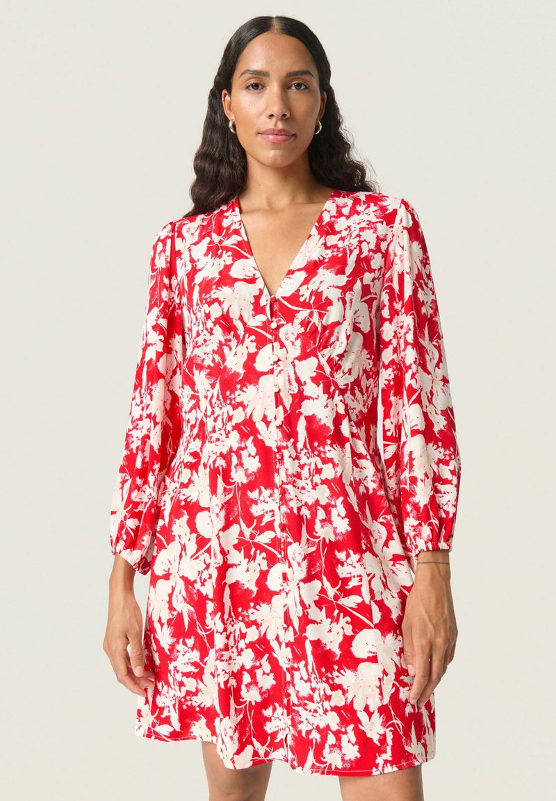 Rotes Blumen-Kleid mit V-Ausschnitt, langen Puffärmeln und lockerem Schnitt. Der Stoff hat eine weiche, strukturierte Optik mit weißen Blumenmustern.