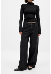 Black long-sleeve fitted top paired with loose, wide-leg black jeans featuring small, subtle dot patterns and a standard waistband. Black pointed flats.