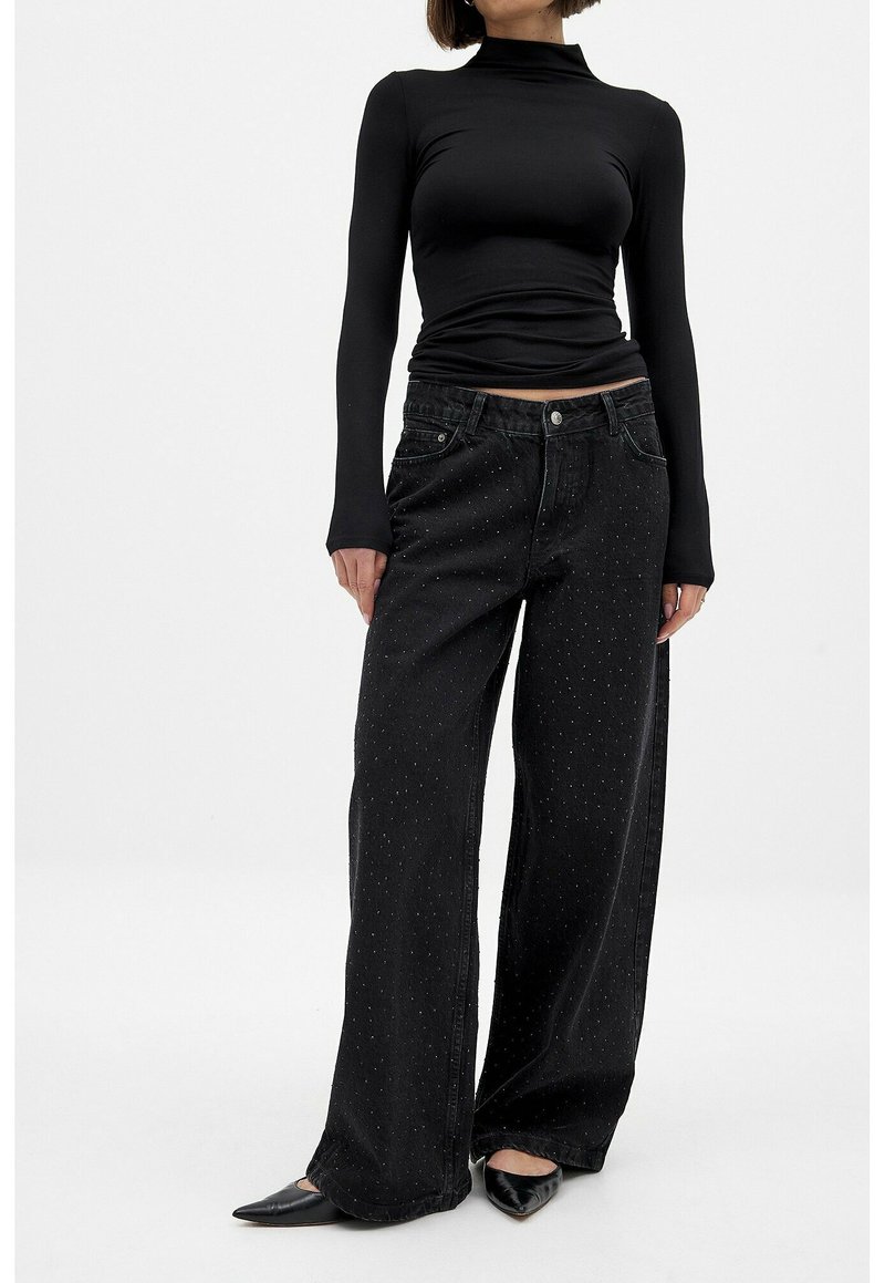 Black long-sleeve fitted top paired with loose, wide-leg black jeans featuring small, subtle dot patterns and a standard waistband. Black pointed flats.