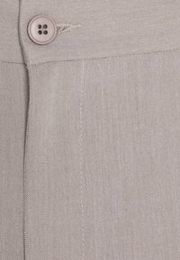 Light beige pants fabric with a sewn button and visible buttonhole near the waistband seam.