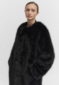 Svart fuskpälsjacka med rund krage, oversized passform och textilstruktur. Slät innervärme och inga synliga hårdvarudetaljer.