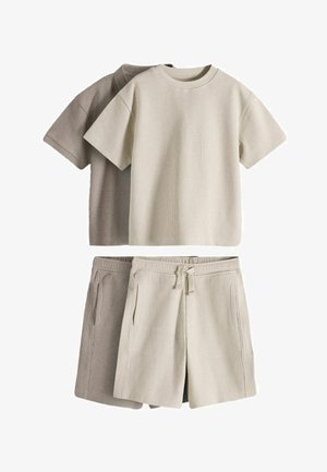 To sæt ribstrikkede kortærmede skjorter og matchende shorts i beige og lys brun lagt fladt på en hvid baggrund.