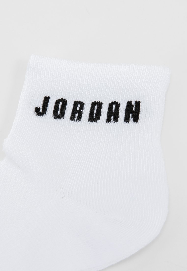 Biała skarpetka do kostki z czarnym napisem "JORDAN" utworzonym po bokach. W fakturze żebrowanej, w tradycyjnym kształcie skarpetki, bez dodatkowych wzorów ani akcentów.