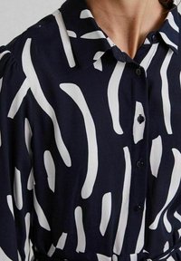 Camicia abbottonata blu navy con motivi astratti a strisce verticali bianche, dotata di colletto e maniche lunghe.