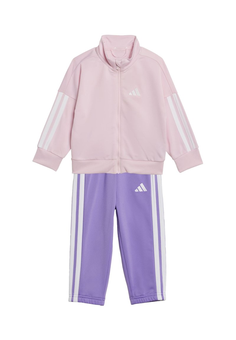 Ljusrosa zip-jacka med vita ränder på ärmarna, tillsammans med lila byxor med vita ränder och en logotyp på båda delarna.