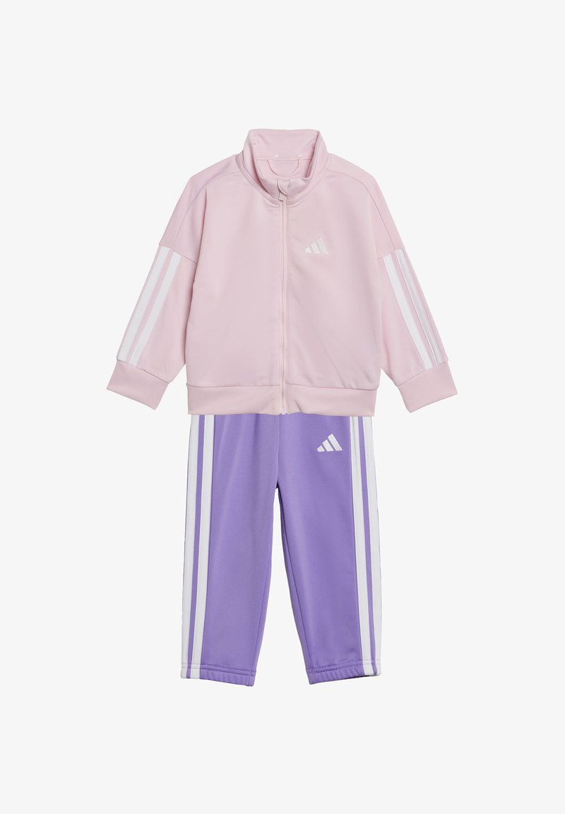 Hellrosa Zip-Jacke mit weißen Streifen an den Ärmeln, kombiniert mit lila Hosen, die ebenfalls weiße Streifen und ein Logo auf beiden Kleidungsstücken haben.