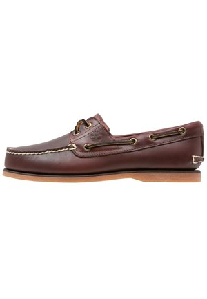 Brown leather boat shoe with a low-profile design, lacing with gold-tone eyelets, and a contrasting tan rubber sole. Stitch detailing is visible.
