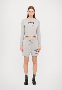 Sweatshirt cropped cinza e calções combinando feitos de um tecido suave, apresentando texto de logótipo preto. Modelo usa meias escuras e sapatos.