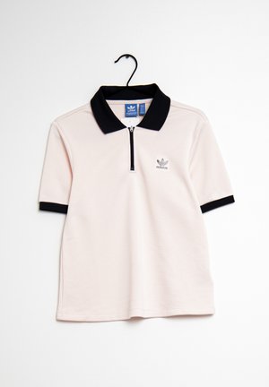 Polo Adidas rose clair avec col noir, poignets des manches noirs, petit logo sur la poitrine, suspendu à un cintre noir sur fond blanc.