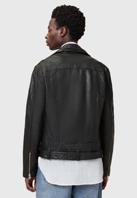 Zwarte leren motorjack met een klassieke kraag, ritssluiting bij de mouwen en een gestructureerde pasvorm, gedragen over een wit shirt.