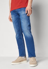 Modré džínové kalhoty s mírným omytem, slim fit a jemným vyblednutím. V kombinaci se světlými béžovými teniskami a červeným tričkem.