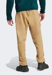 Beige Outdoor-Hosen mit einem lockeren Schnitt, ausgestattet mit einer glatten Textur und einem elastischenBund, kombiniert mit schwarzen Wanderschuhen.