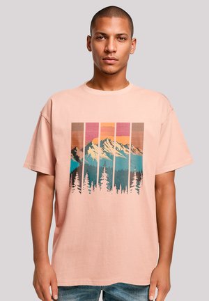 Pink cotton t-shirt featuring a mountain landscape graphic in blue, brown, and pink hues, with a loose fit and short sleeves.