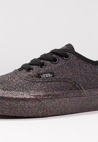 Svarta Vans-sneakers med en glittrig textur som har en flerfärgad glittrande effekt, svarta snören och en liten logotag på sidan.
