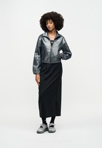 Metalna srebrna kratka jakna s elastičnim strukom, uparena s crnom midi suknjom s bočnim prorezom. Sivi slip-on cipele zaokružuju izgled.