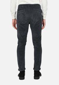 Pantaloni in corduroy grigio scuro a vestibilità slim, con due tasche posteriori e risvolti. Texture morbida e motivo a righe verticali visibile.