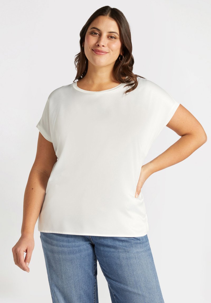 Weißes, kurzärmliges Oberteil mit einer weichen, glatten Textur und Rundhalsausschnitt, ergänzt durch eine lässige Passform. Kombiniert mit blauen Jeans.